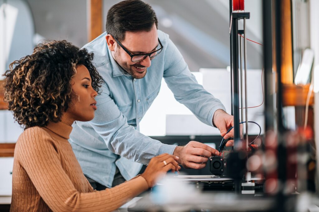 Technology, people and engineering concept. Handsome man learning woman how to use 3D printer.